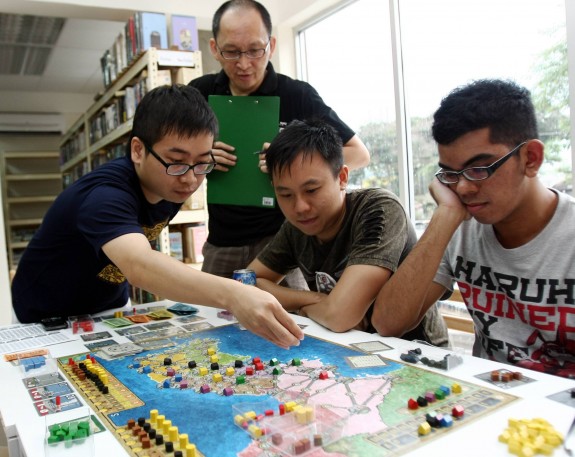 CK Au (holding the file) monitors the Power Grid session intently in the recent Power Grid boardgame competition finals, held in Boardgame Depot, Bangsar. Matthew Goh (centre) was the big winner