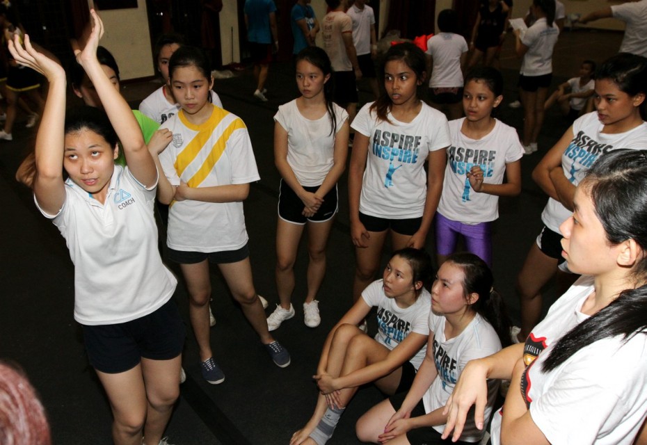 Coach Lim Cheng Choo (left) showing cheerleaders how to hold a flyer’s shoe during training.