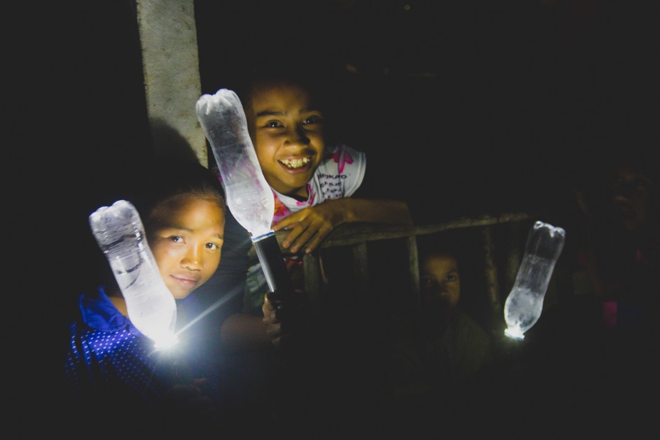 The children of Kampung Lemoi are all smiles as they stand next to their brand new solar powered water bottle lamps. Kampung Lemoi had long been plunged in darkness, and villagers resorted to old-fashioned light sources like bonfires to get some light. - Photo: Joe Kiat